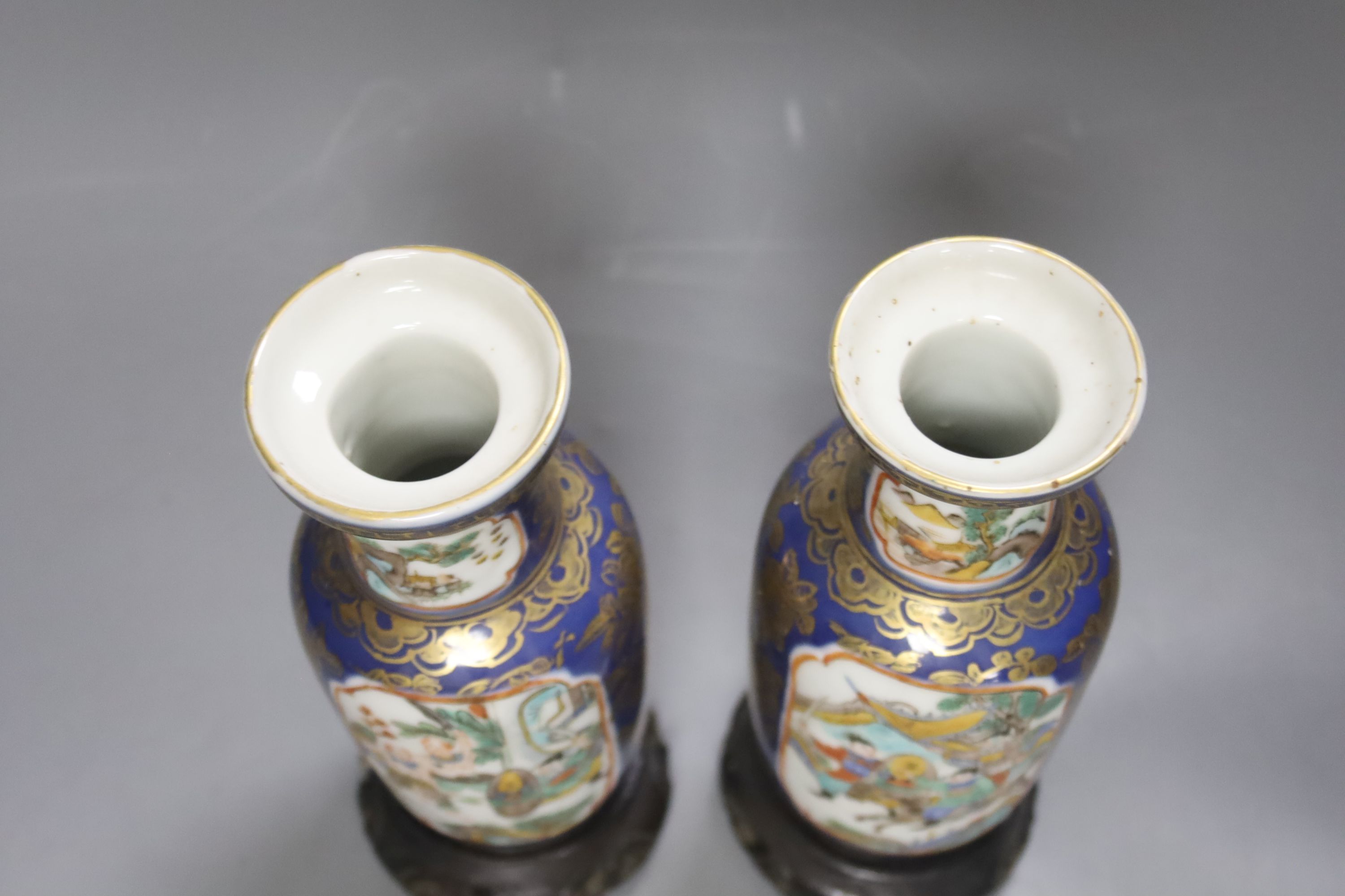 A pair of Chinese Kangxi style blue-ground vases, late 19th century decorated with panels of warriors and heightened in gilt, on carved hardwood stands, height 18cm excluding stand